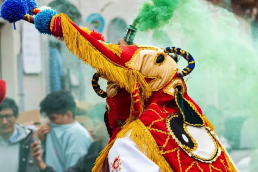 Danzante de traje rojo con flecos dorados agitando un fuete de pompones entre humo verde