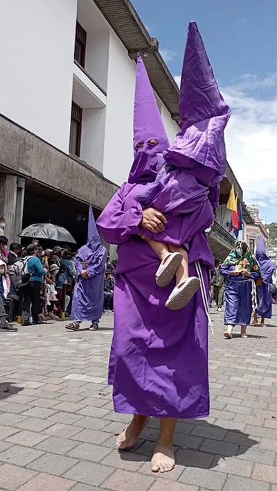Un cucurucho descalzo carga en brazos a un niño, también vestido de penitente, durante la procesión
