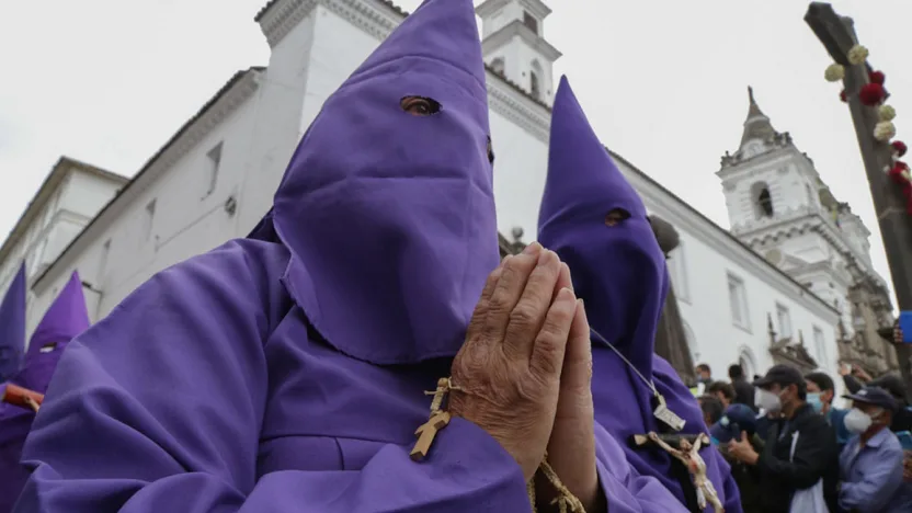 Dos cucuruchos con hábito morado y las manos juntas en oración durante la procesión