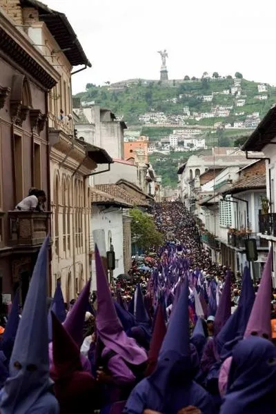 Calle colonial de Quito colmada de cucuruchos morados, con El Panecillo al fondo