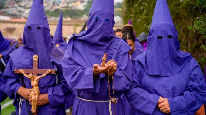 Primer plano de tres cucuruchos sosteniendo un crucifijo y un rosario