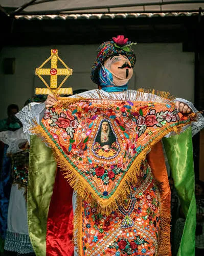 Danzante sosteniendo en alto una cruz dorada y un pañolón bordado con la imagen de la Virgen