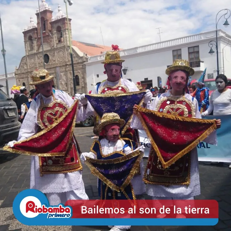Danzantes de Yaruquíes, adultos y un niño, posando con sus pañolones frente a la fachada de piedra de la Catedral de Riobamba