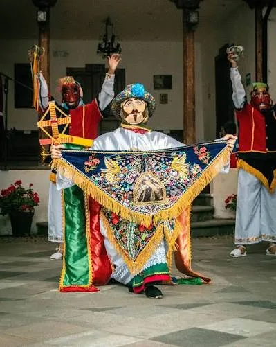 Tres danzantes de Yaruquíes; el del centro, arrodillado, despliega un gran pañolón bordado con un sol dorado