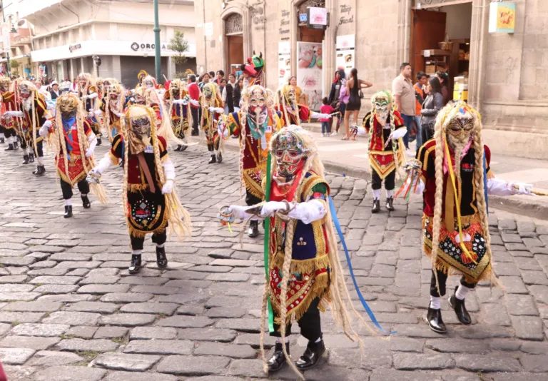 Comparsa de Diablos de lata danzando sobre la calle empedrada del centro de Riobamba