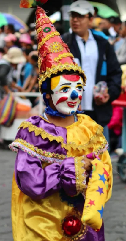 Payaso con gorro cónico rojo y dorado, rostro pintado de blanco y traje morado con amarillo